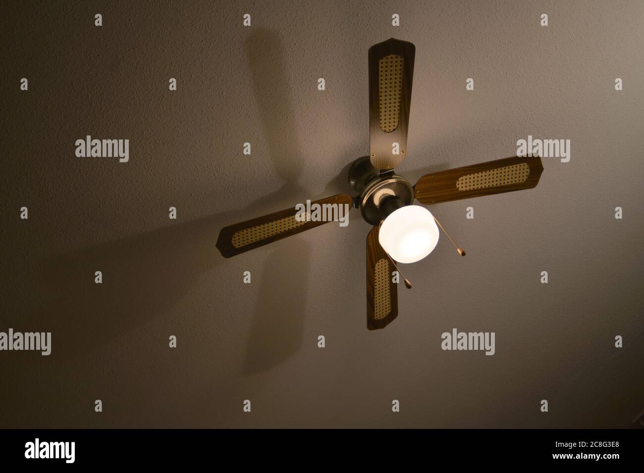 Mediterranean brown wood and material ceiling fan casts a long shadow on a plaster ceiling. Stock Photo