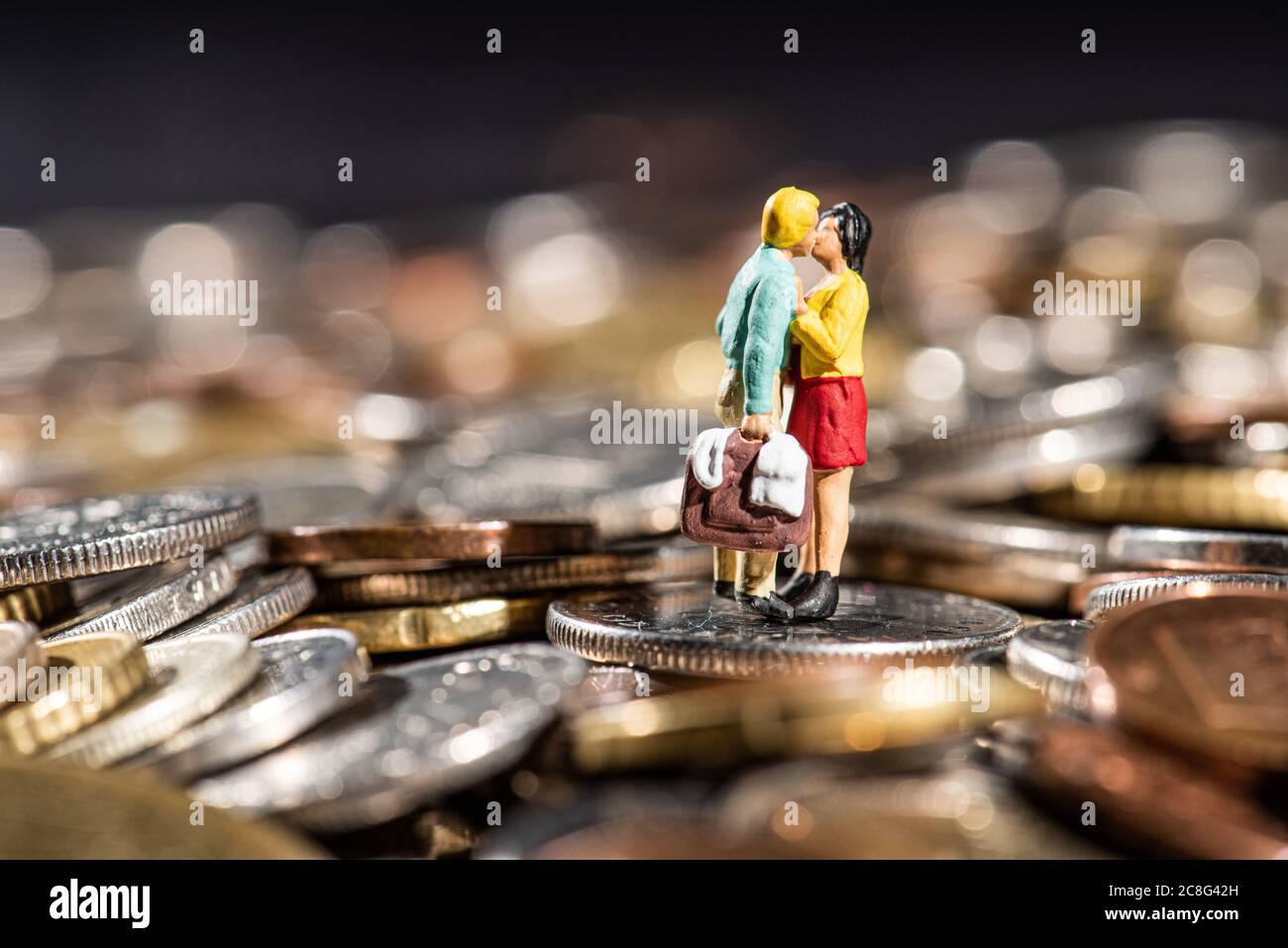 Small figures of a gouple kissing standing on a pile of coins. Stock Photo