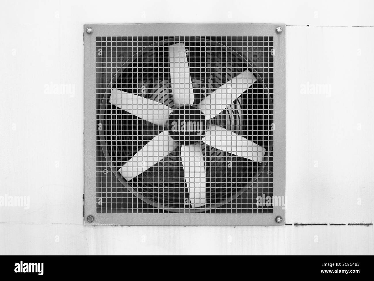Ventilator behind grid. Device for regulation of heat and wind. Blades of ventilation system are white. Black and white shot Stock Photo