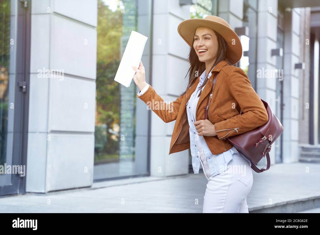 Travelling making us happy. Young and beautiful cheerful female traveler or tourist wearing hat and backpack holding map and smiling while walking on city street. Vacation, trip. Traveling and tourism Stock Photo