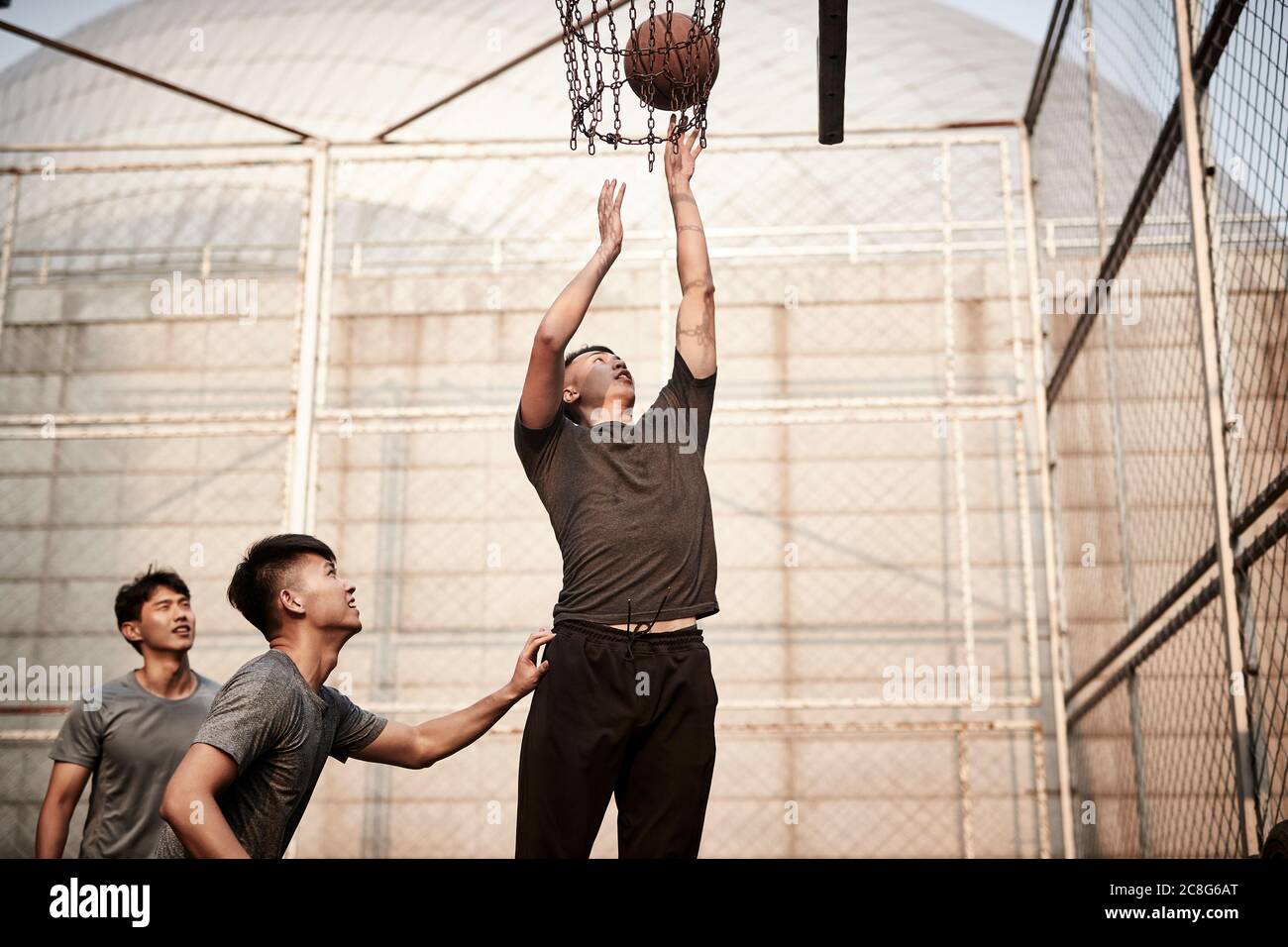 young asian adult men playing basketball on outdoor court Stock Photo