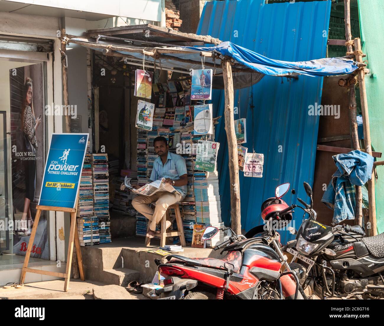 Trichy, Tamil Nadu, India - February 2020: A shopkeeper reading a newspaper inside a roadside bookshop on the market streets of Tiruchirappalli. Stock Photo