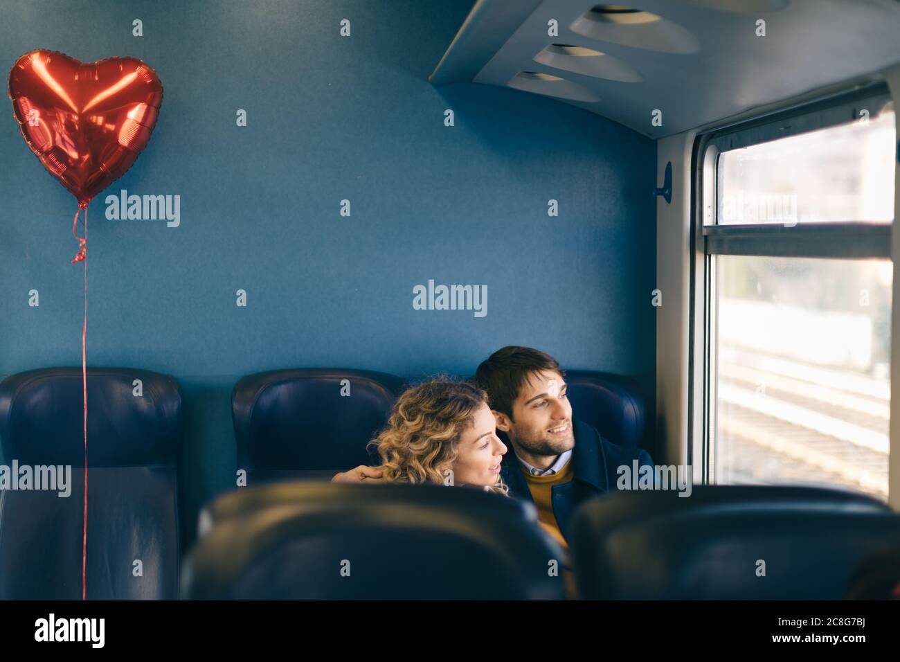Couple with heart shaped balloon looking out window of train Stock Photo