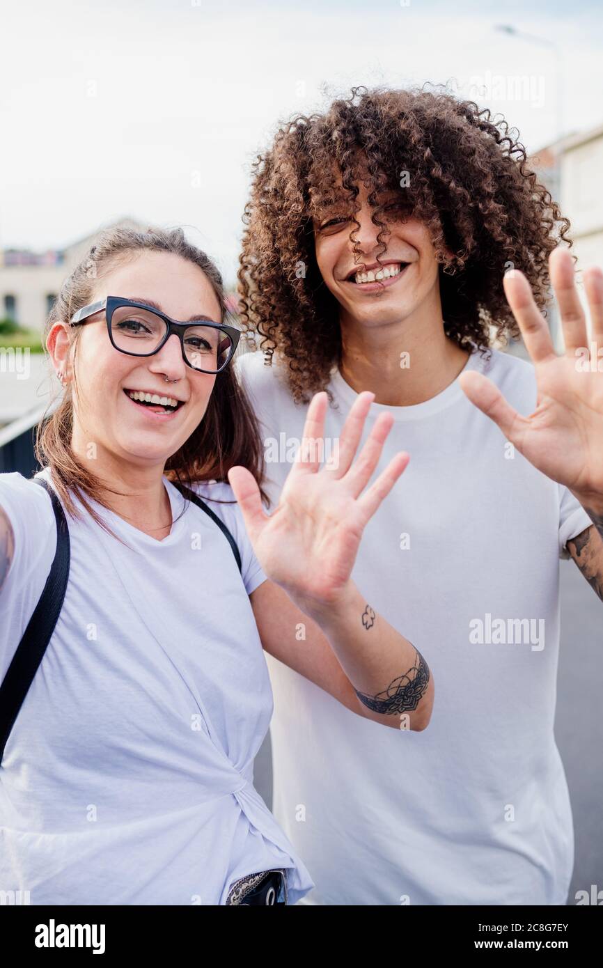 Portrait of woman and man with tattooed arms, smiling and waving at camera. Stock Photo
