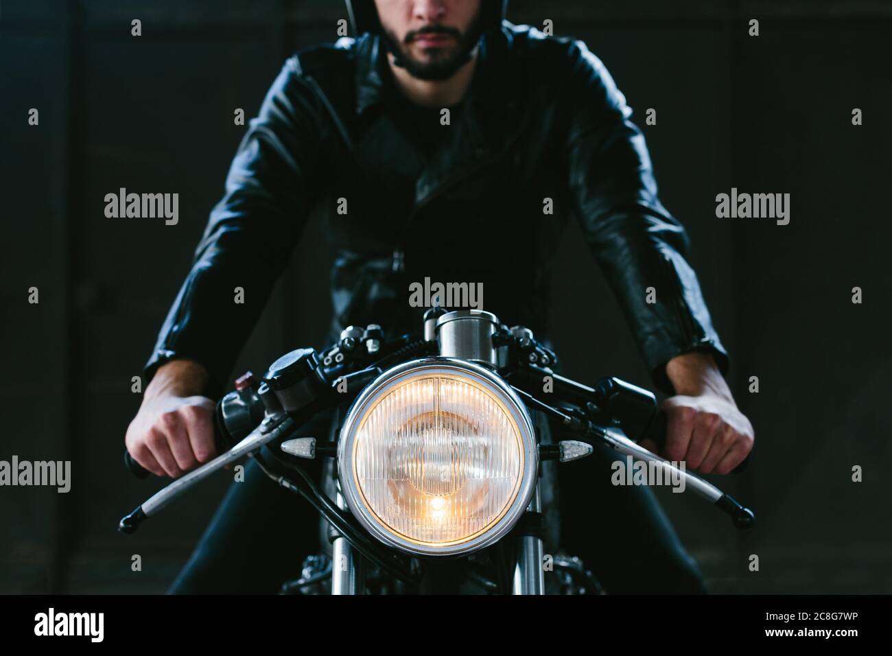 Moto Straddle Young male motorcyclist straddling vintage motorcycle in garage ...