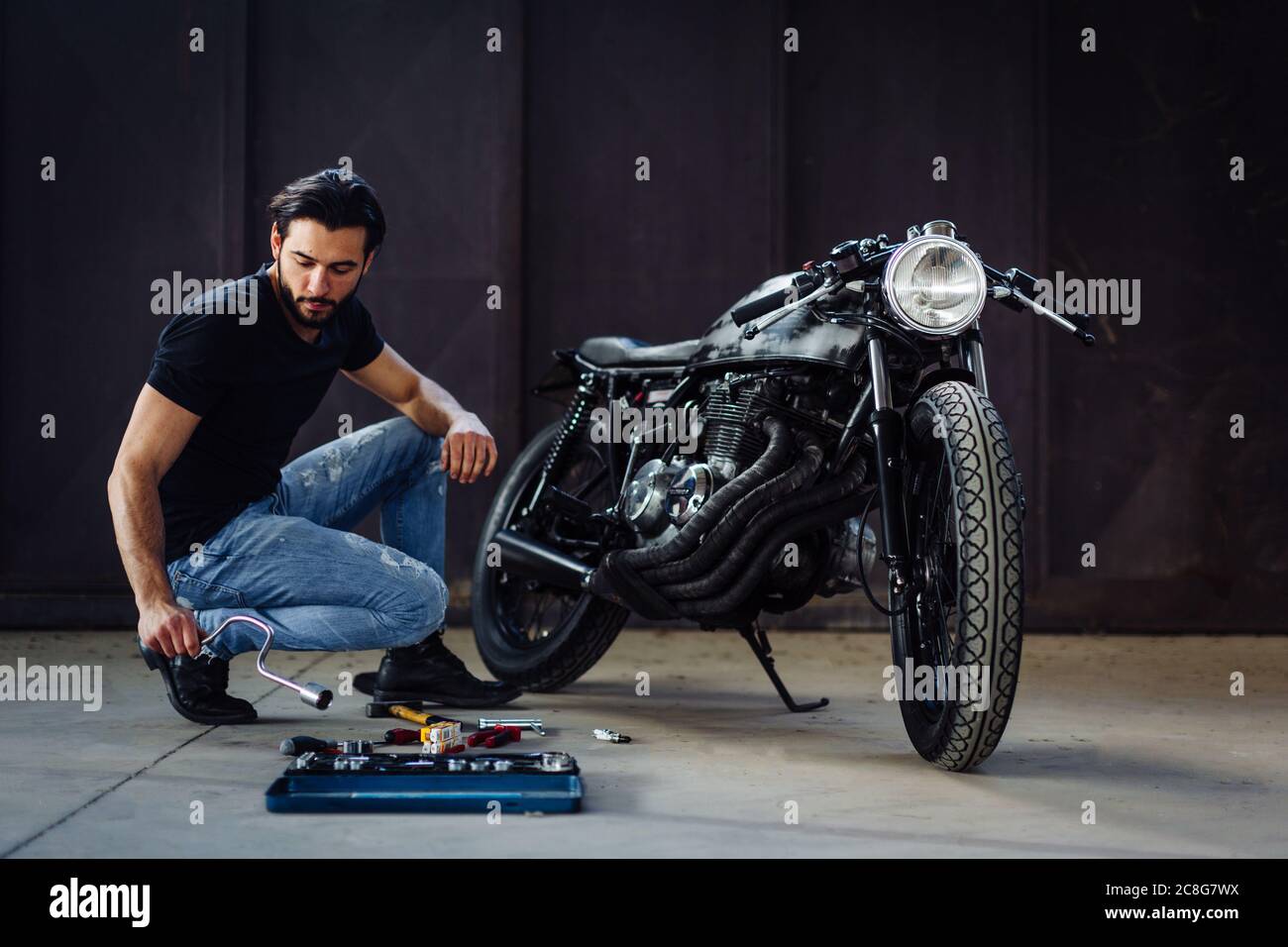 Young male motorcyclist doing maintenance on vintage motorcycle in garage Stock Photo