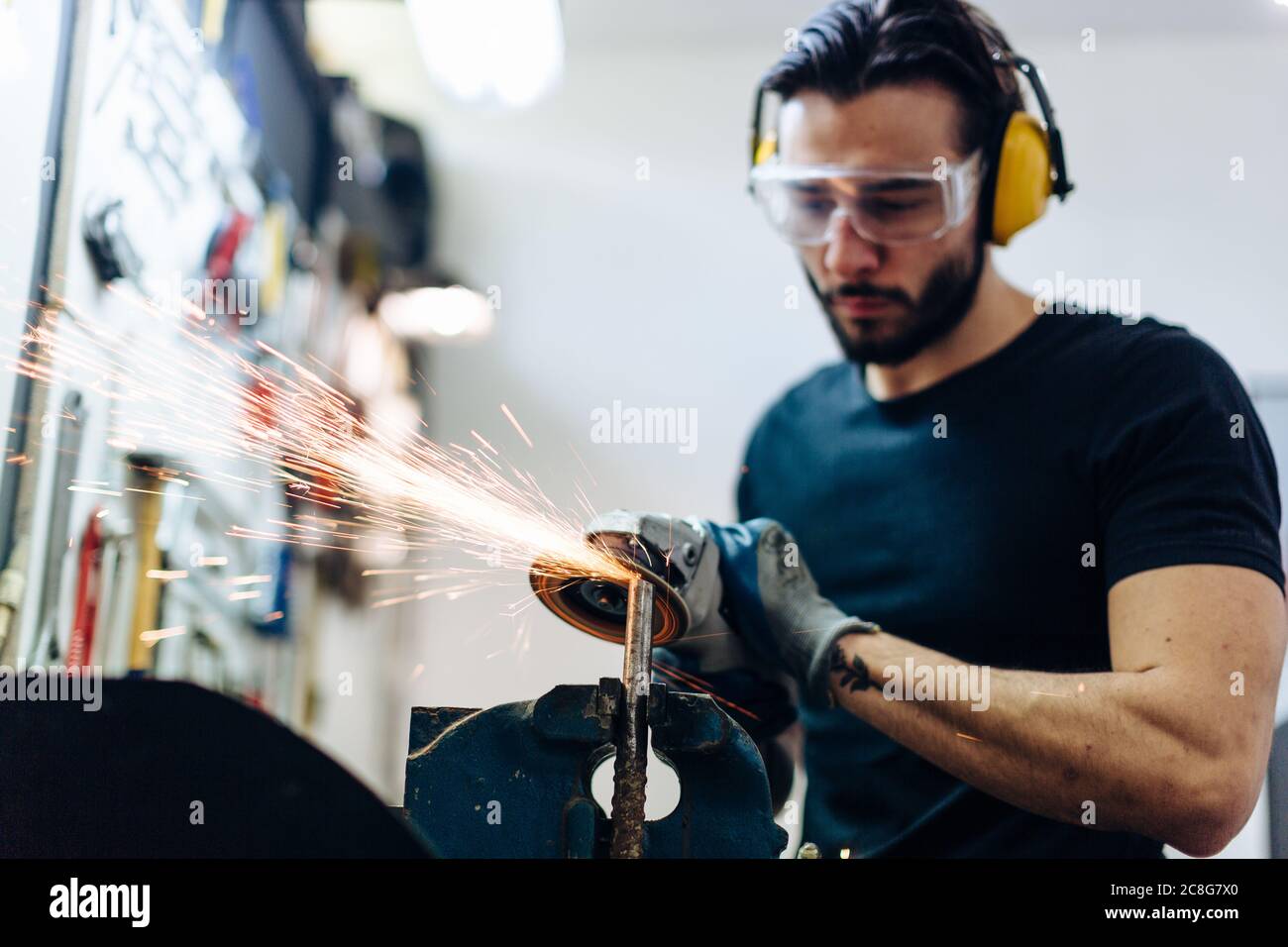 Young man using angle grinder on metal in workshop Stock Photo