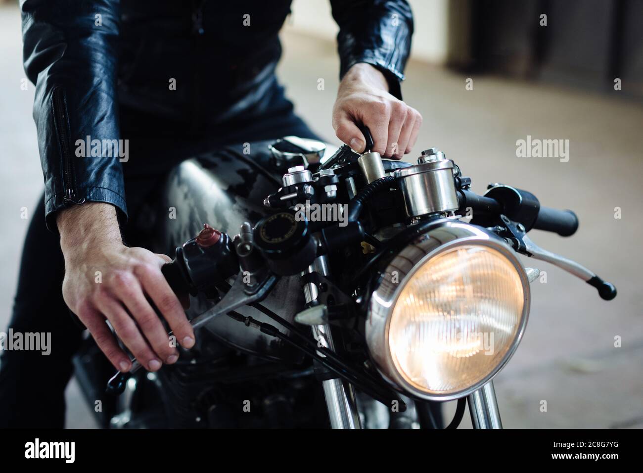 Young male motorcyclist straddling vintage motorcycle in garage, cropped Stock Photo