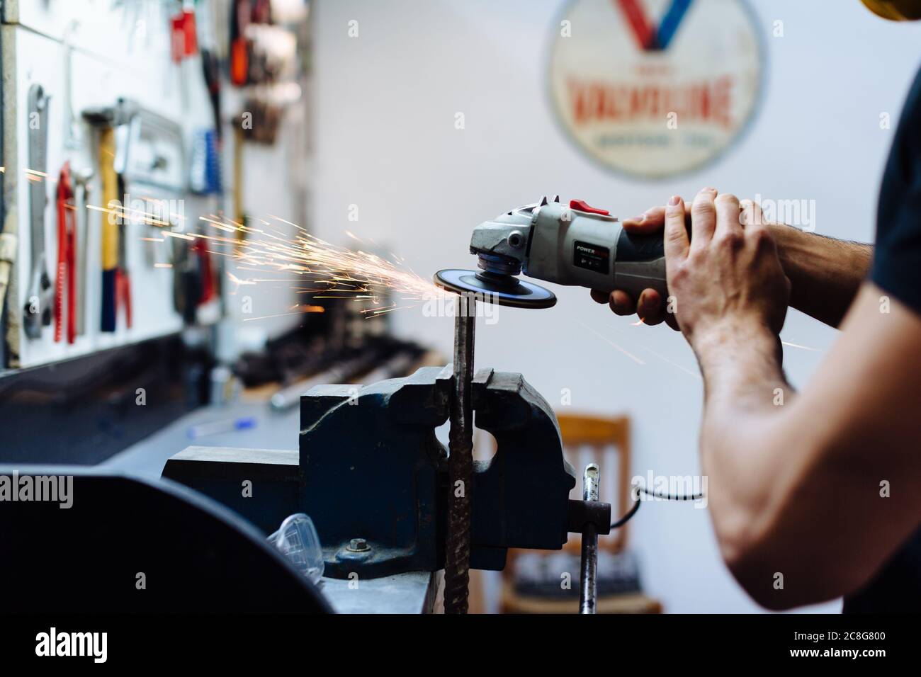 Young man using angle grinder on metal in workshop, cropped Stock Photo