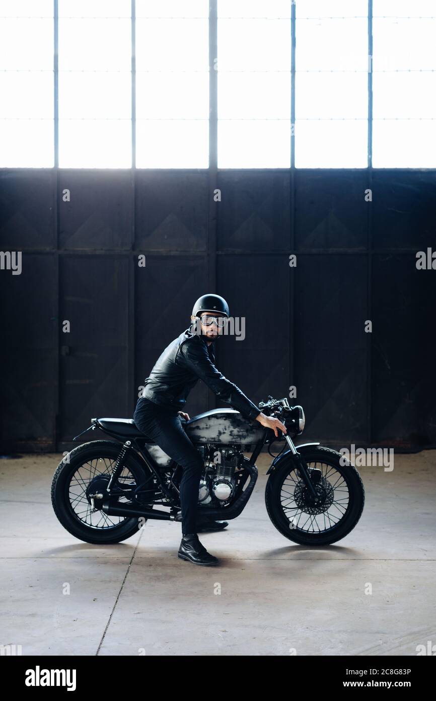 Young male motorcyclist on vintage motorcycle in empty warehouse, portrait Stock Photo