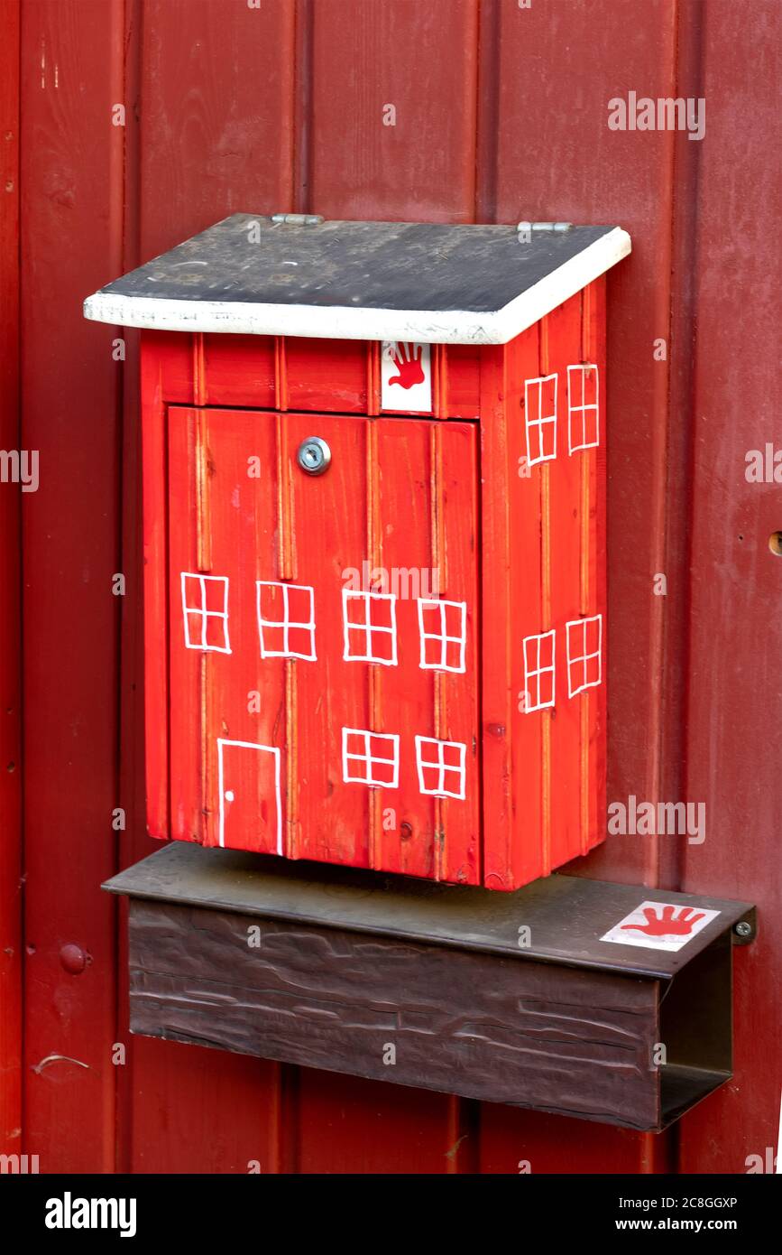 Red mailbox with small painted windows and door on a red wooden house wall Stock Photo