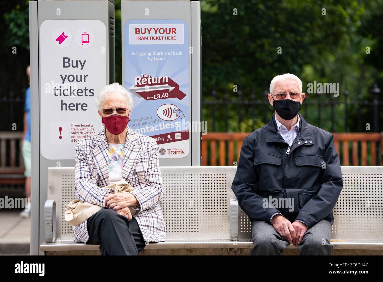 Edinburgh, Scotland, UK. 24 July, 2020. Senior couple sitting at tram stop social distancing themselves and wearing facemasks.  Iain Masterton/Alamy Live News Stock Photo