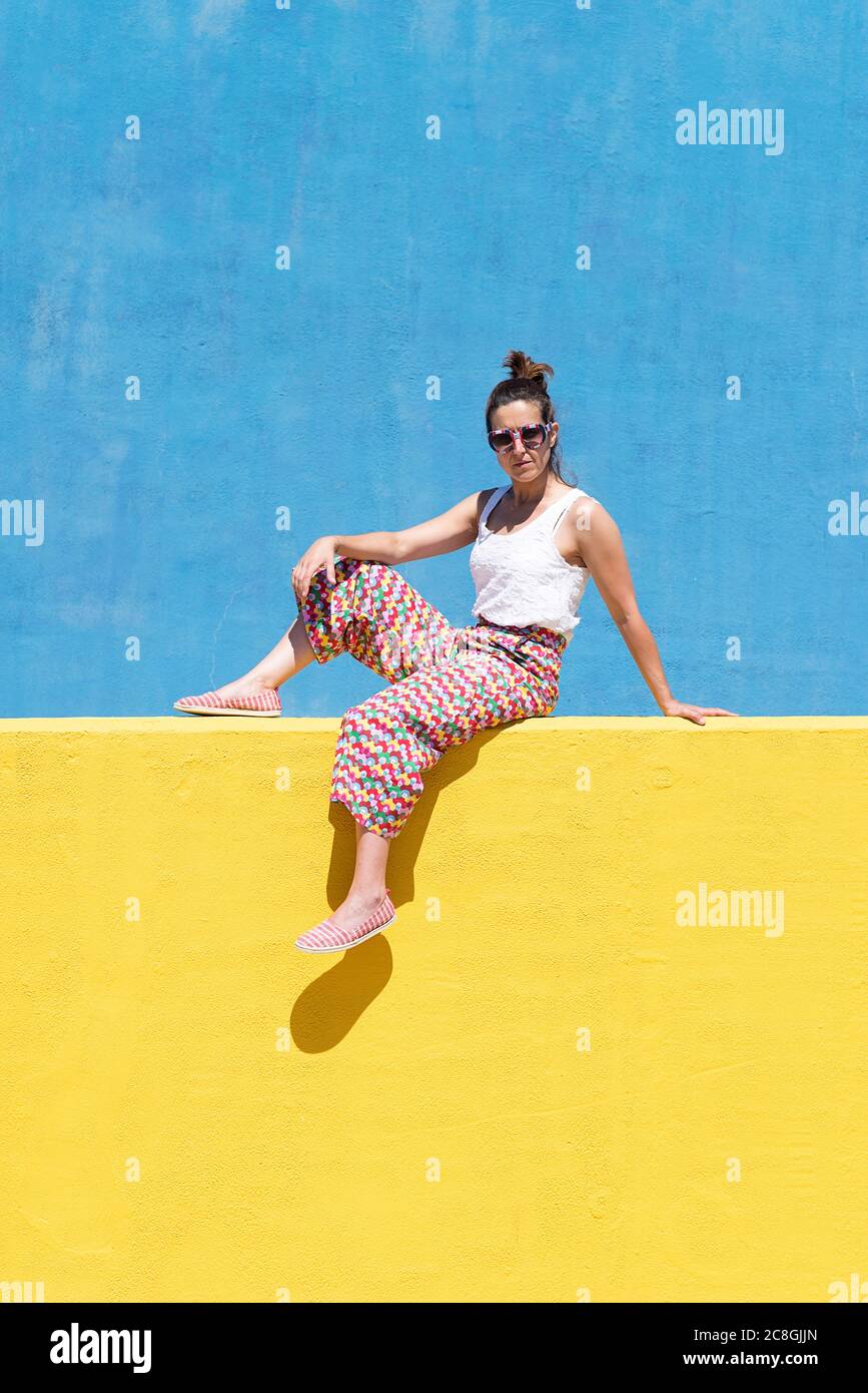 Trendy woman sitting on yellow wall while taking a selfie Stock Photo ...