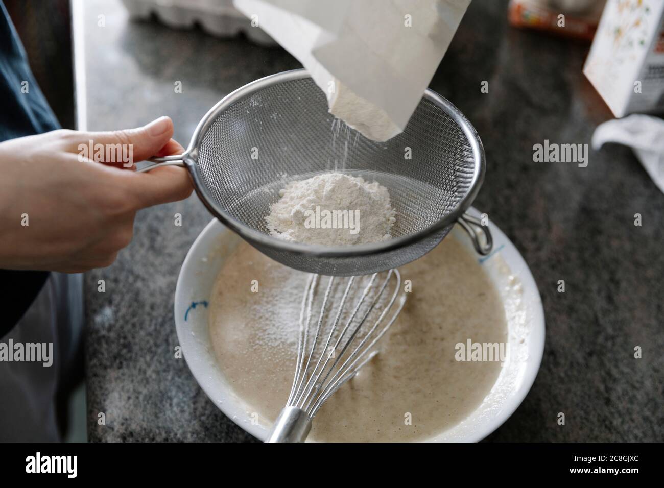 High angle of crop person sieving flour for cooking pastry in kitchen