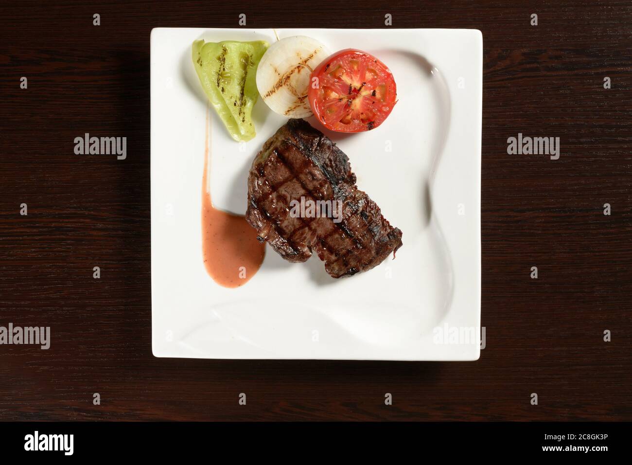 Roasted meat of marble beef steaks with grilled vegetables of tomato, onion and bell pepper on a square plate on a wooden table. Top view. Photos for Stock Photo