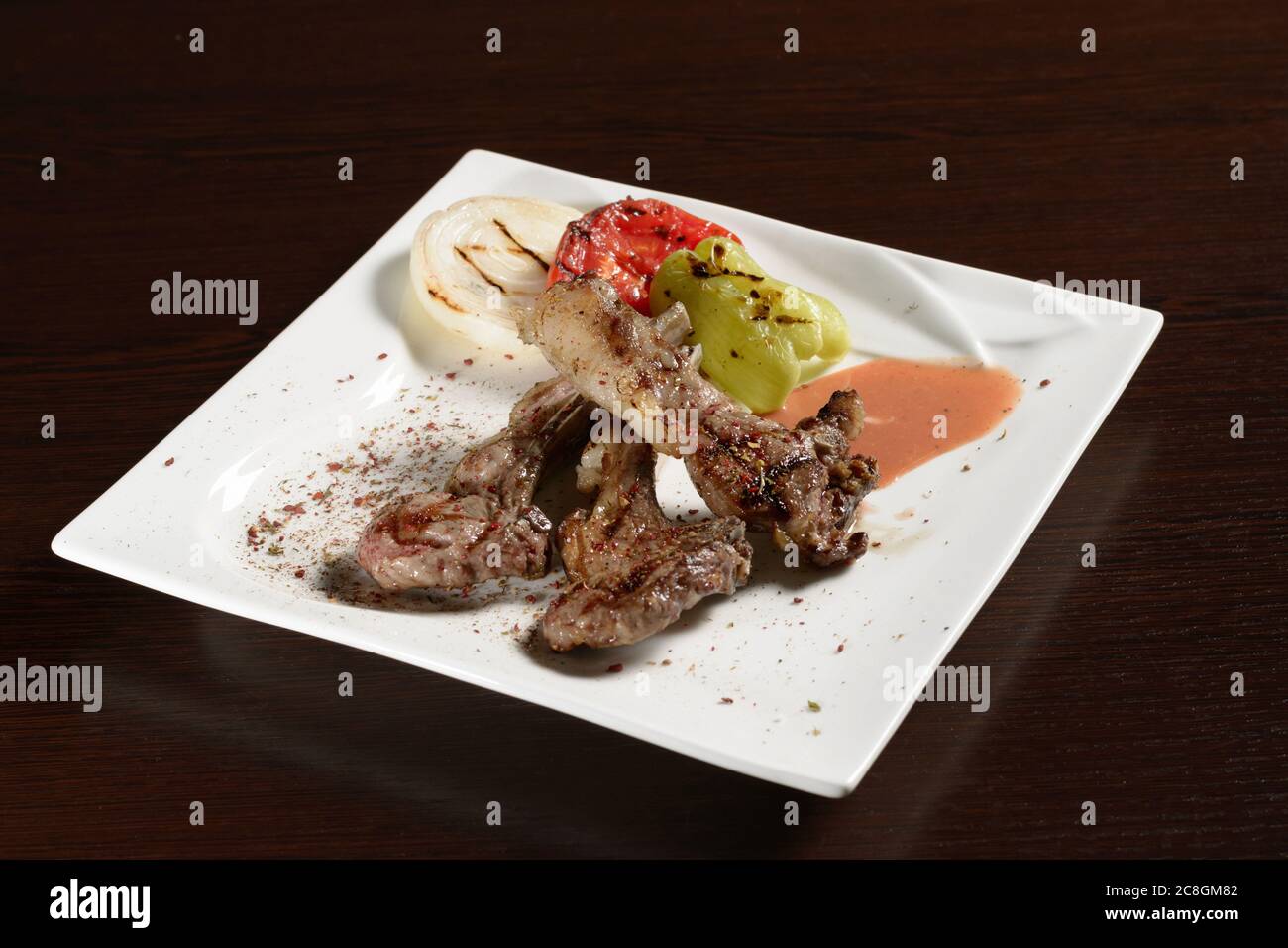Вarbecue beef ribs with grilled vegetables of tomato, onion and bell pepper on a square plate on a wooden table. Photos for restaurant and cafe menus Stock Photo