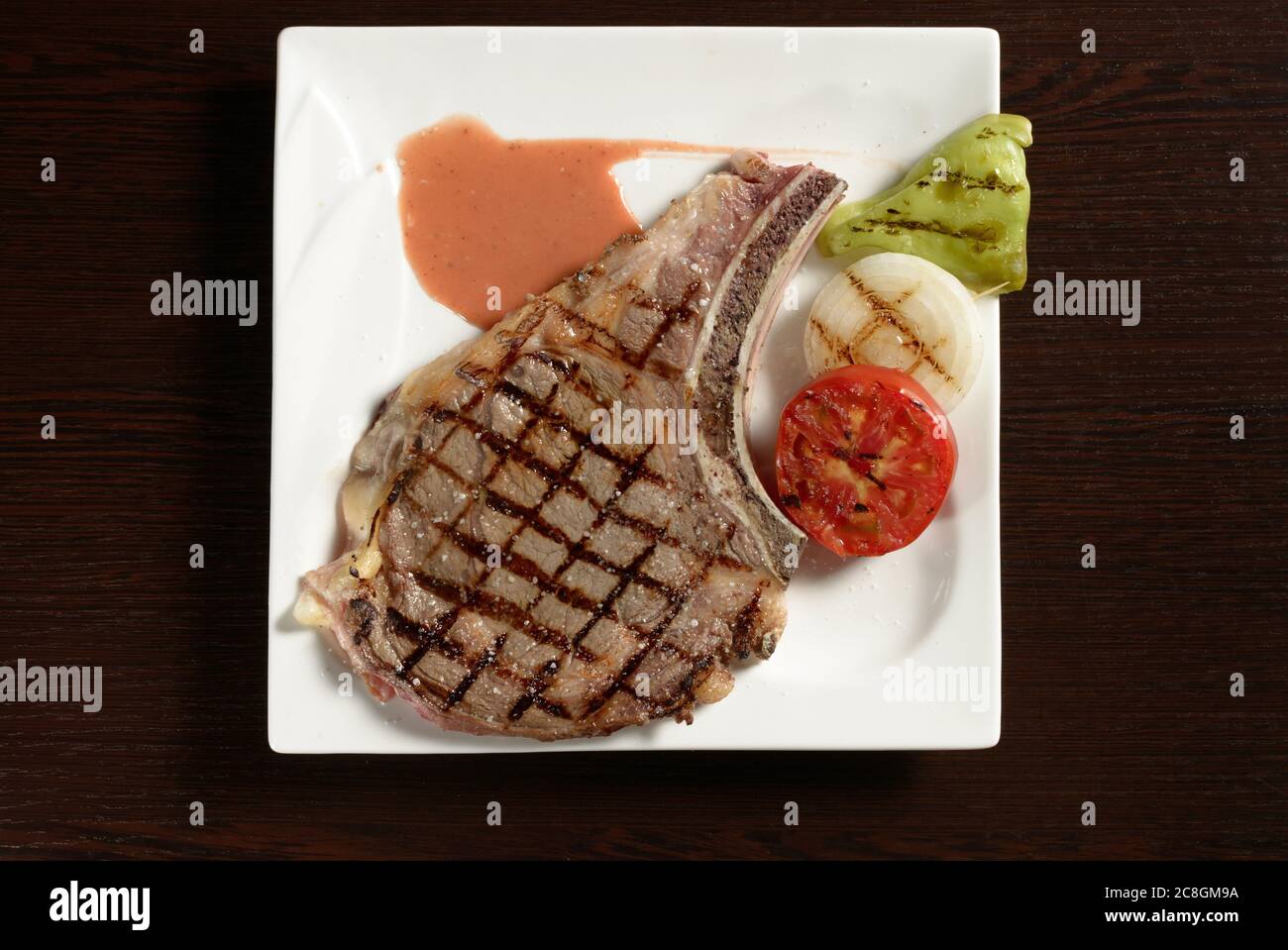 Grilled cowboy beef steak with grilled vegetables of tomato, onion and bell pepper on a square plate on a wooden table. Top view. Photos for restauran Stock Photo