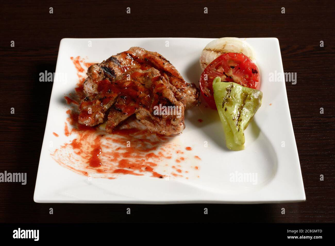 Barbecue chicken wings with grilled vegetables of tomato, onion and bell pepper on a square plate on a wooden table. Photos for restaurant and cafe me Stock Photo