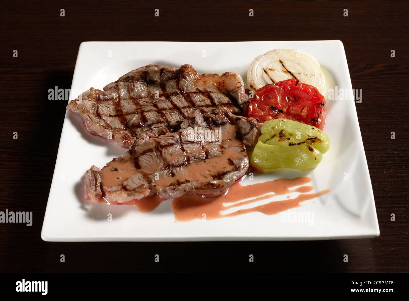 Beef tenderloin barbecue steak with grilled vegetables of tomato, onion and bell pepper on a square plate on a wooden table. Photos for restaurant and Stock Photo