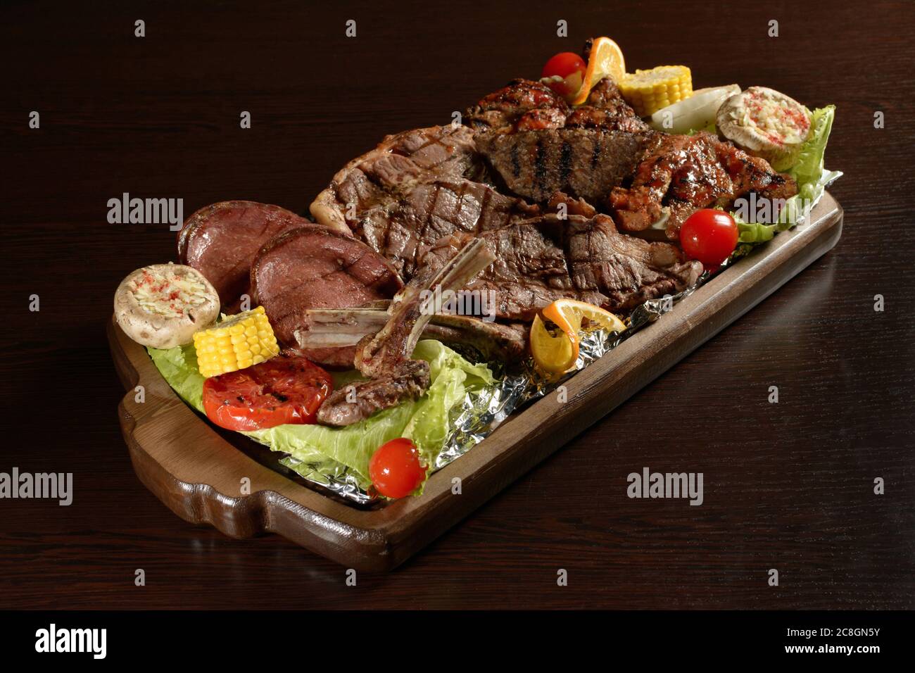 Meat assortment of barbecue meat with vegetables on a rustic tray and wooden table Stock Photo