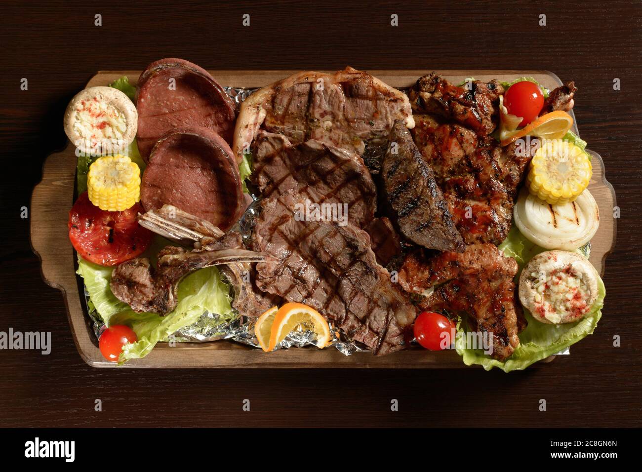 Assortment of grilled meat with vegetables on a rustic tray and wooden table Stock Photo