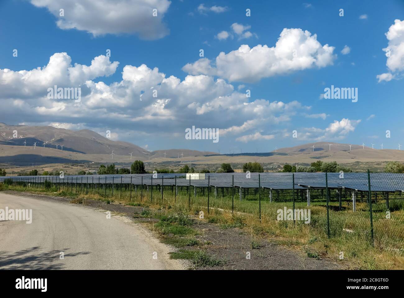 Power generation plant, with several solar panels and wind turbines in the background, commune of Pescina, Abruzzo region, province of Aquila, Italy Stock Photo