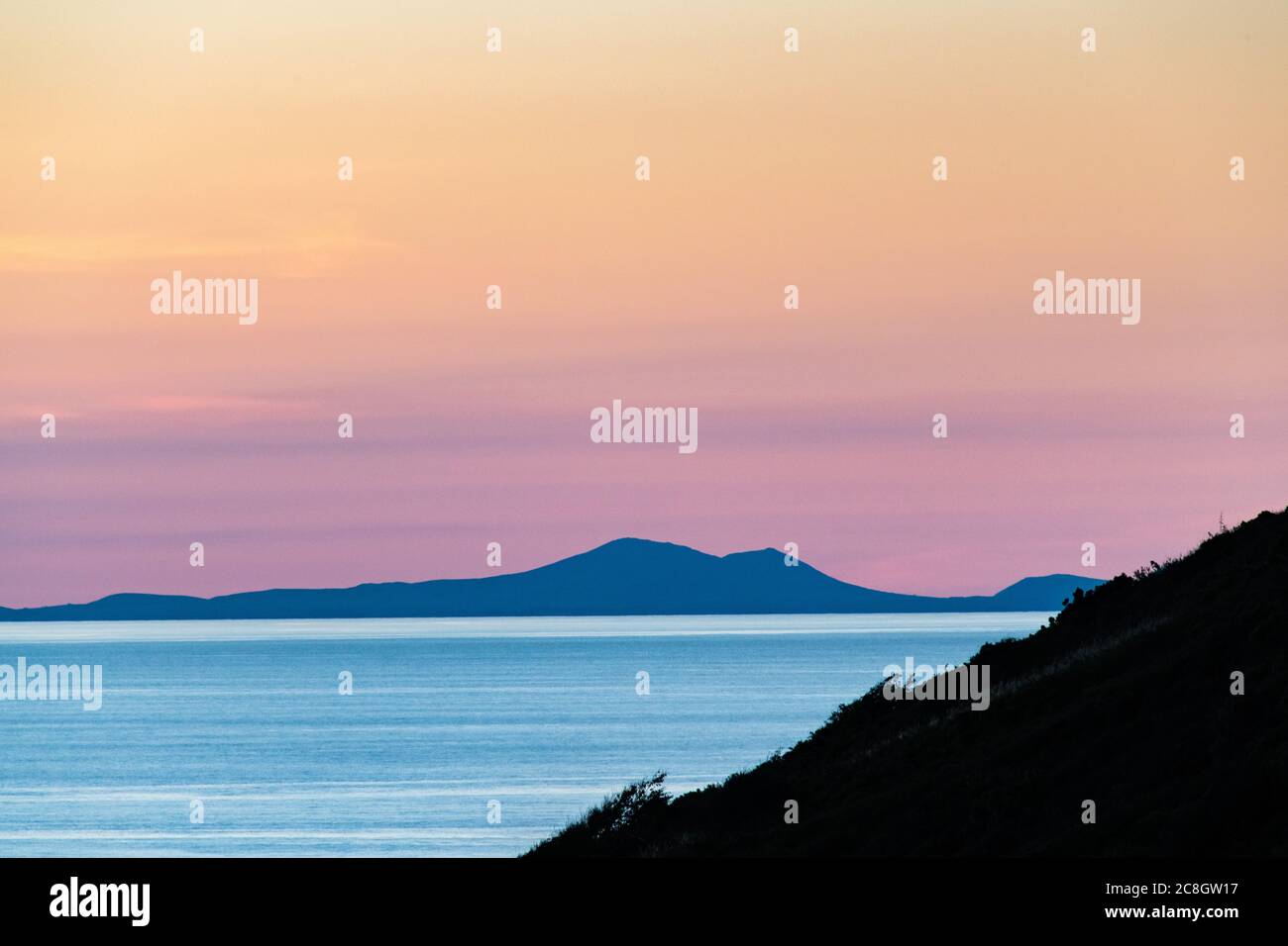 A tranquil Cardigan Bay sunset view taken from Pen Dinas Hill Fort in Aberystwyth with the Llyn Peninsula in the distance in a warm summer time  glow. Stock Photo