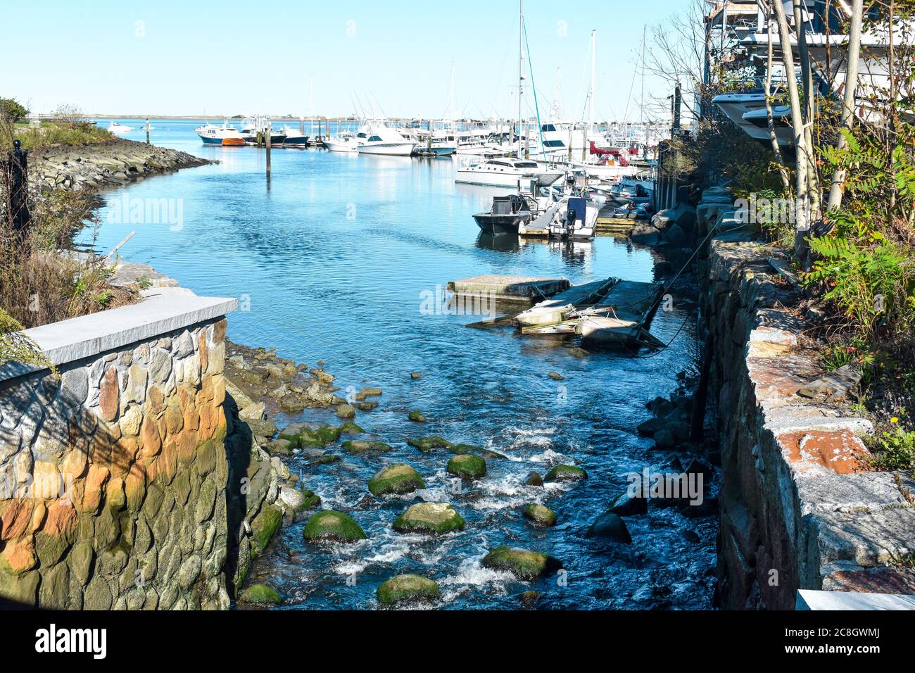 Town Brook flowing over rocks into Pymouth Harbor near boats at the Plymouth Marina Stock Photo