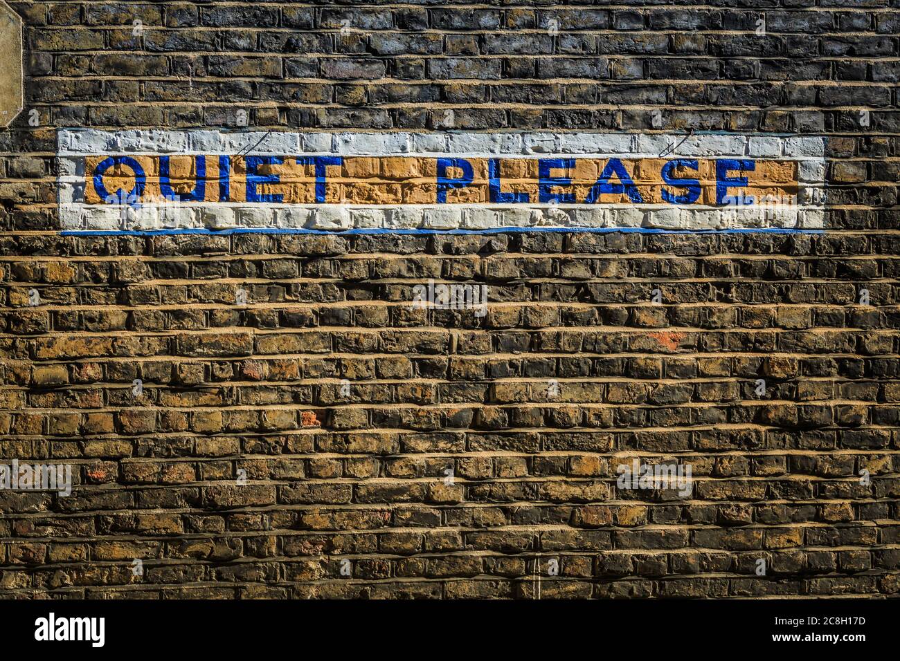 Grungy brick wall with the words 'Quiet Please' painted/written in block letters on a city wall.  Taken in London. Stock Photo