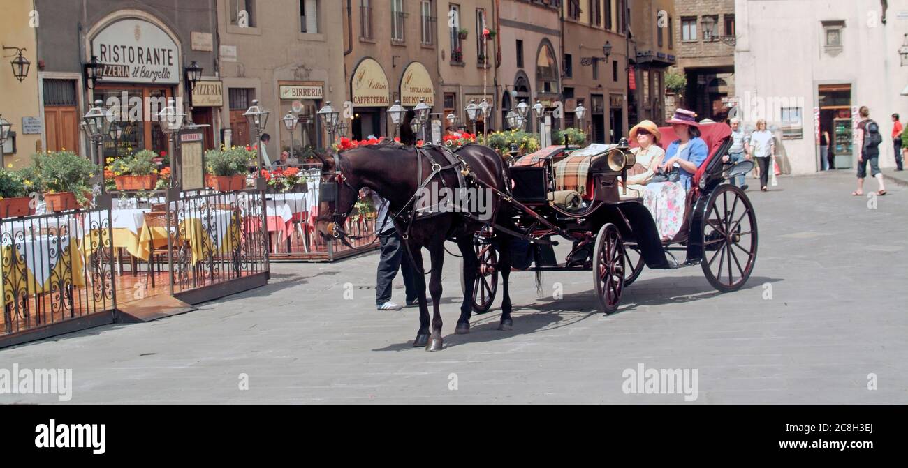 Italian horse drawn open carriage two women passengers arriving at pavement bars & Ristorante in sunny Piazza della Signoria Florence Tuscany Italy EU Stock Photo