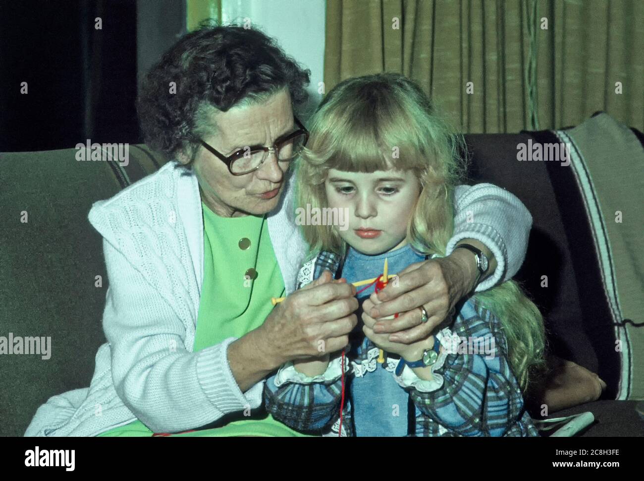 Concentration of young girl child granddaughter & grandmother gets help learning knitting  from old senior mature granny grandparents home indoors UK Stock Photo