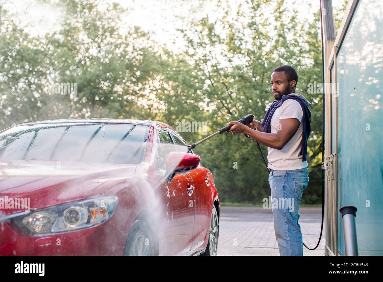 Optage Akvarium afregning Car wash service outdoors. African guy in white t-shirt and jeans, washing  red luxury car with water gun on an open air self car wash Stock Photo -  Alamy