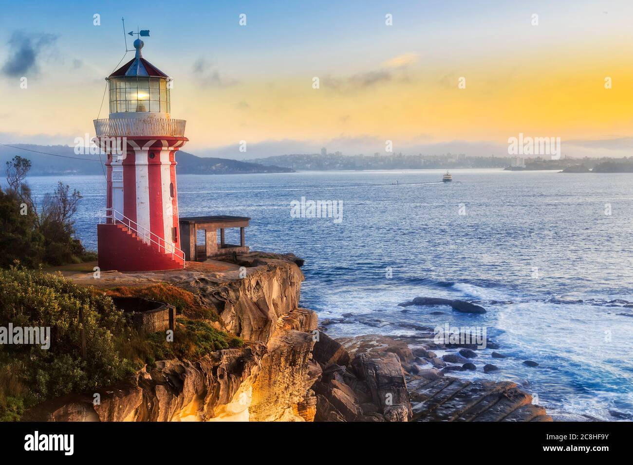 Hornby lighthouse and ferry from Sydney to Manly at sunrise on the edge of sandstone rock near Sydnay harbour entrance. Stock Photo