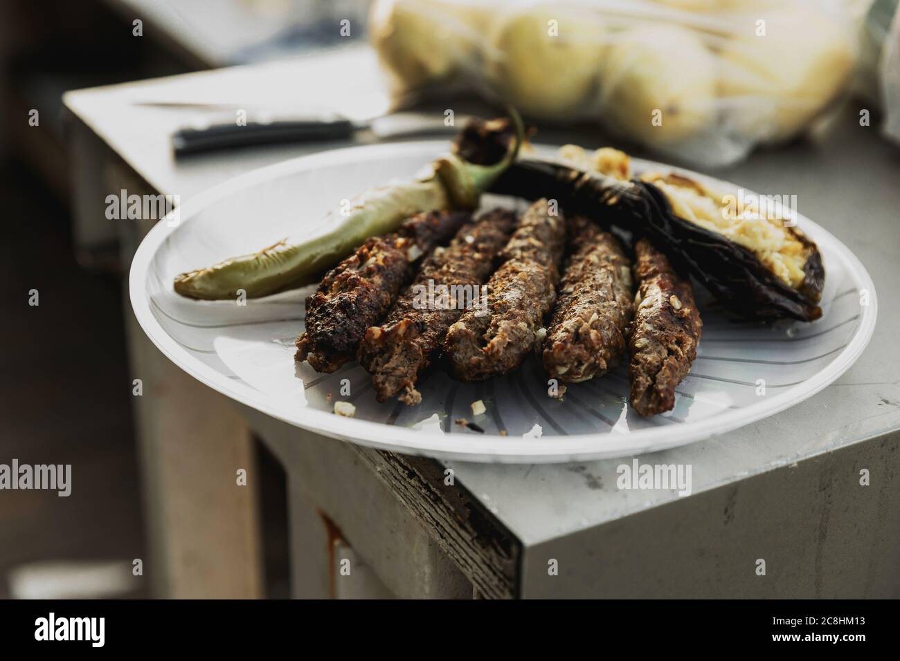 Cooked kebabs, green hot peppers and eggplant on a disposable plate on the street outdoor. Summer barbecue cooking. BBQ on the terrace. Party time, le Stock Photo