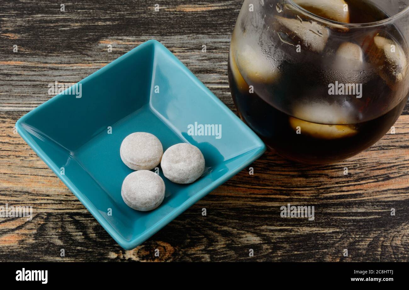 Cola flavored hard candy in blue candy dish with glass on cola with ice