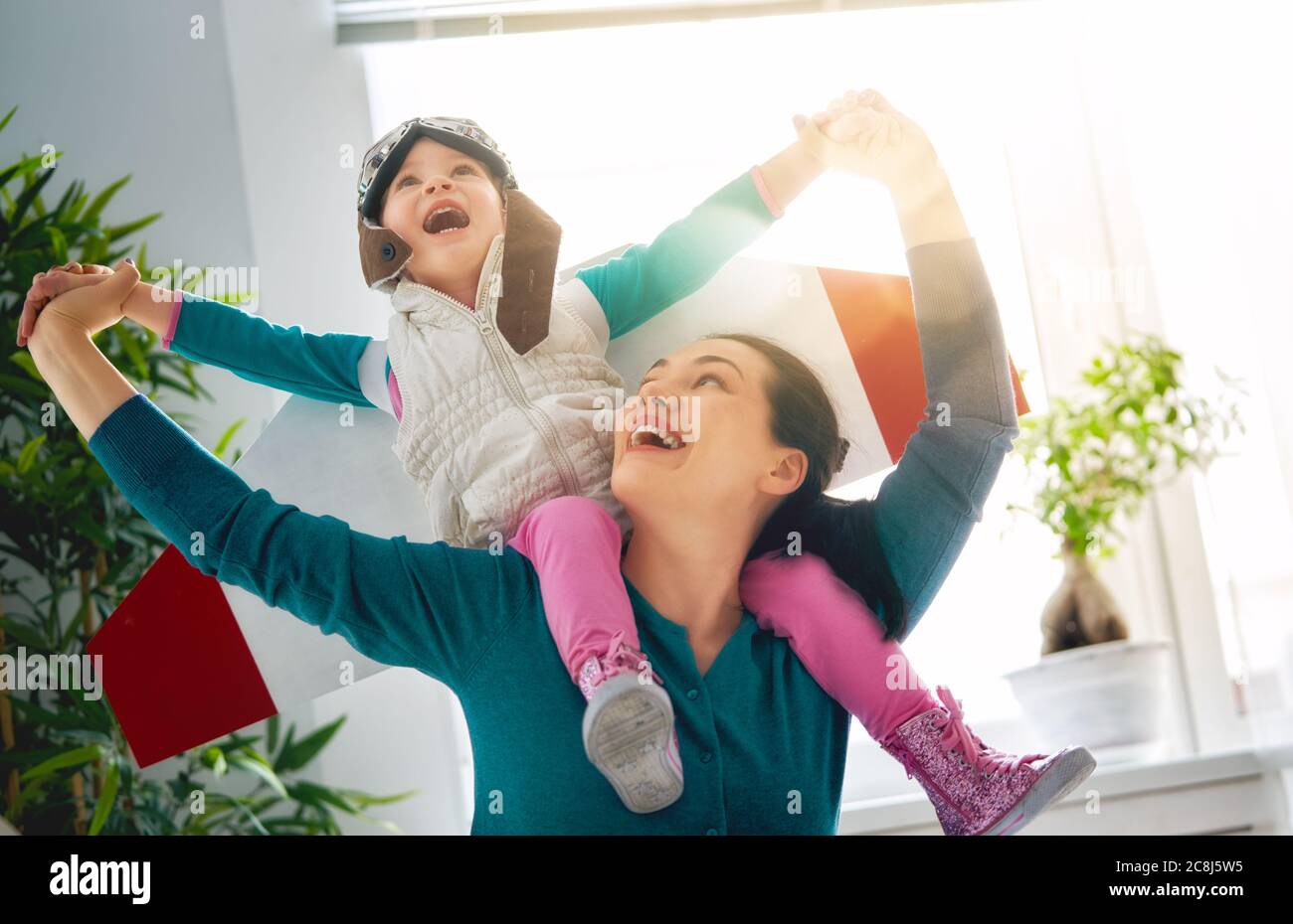 Happy family is having fun at home. Mother and her child girl playing together. Girl in pilot's costume. Stock Photo
