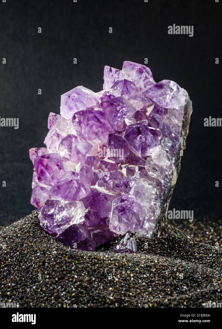 Amethyst gemstone closeup placed on black sand. Mineral is showcased in a volcanic natural feeling like environment Stock Photo