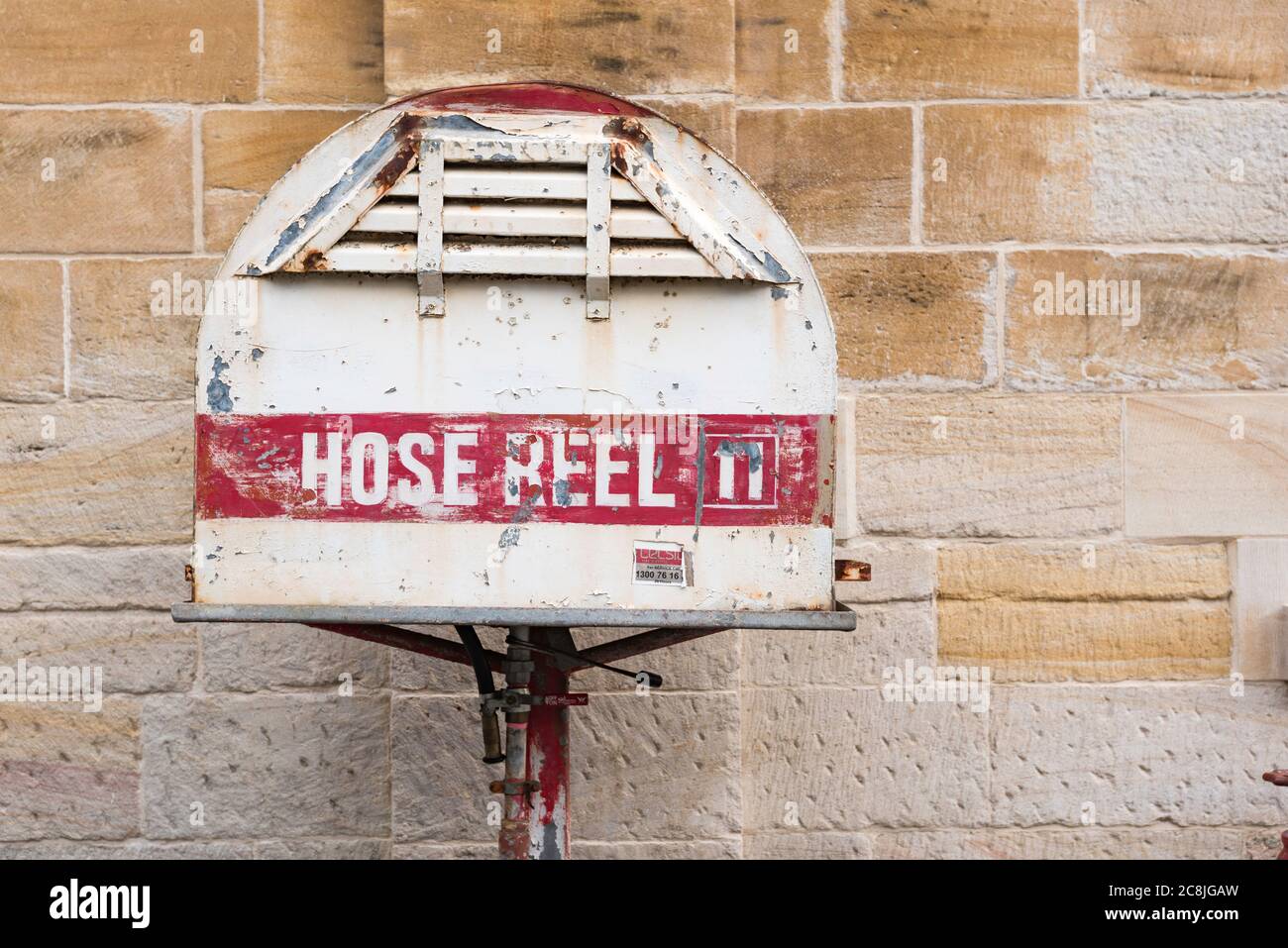 An old red and white painted fire hose reel standing in front of a sandstone wall on Cockatoo Island in Sydney Harbour, New South Wales, Australia Stock Photo
