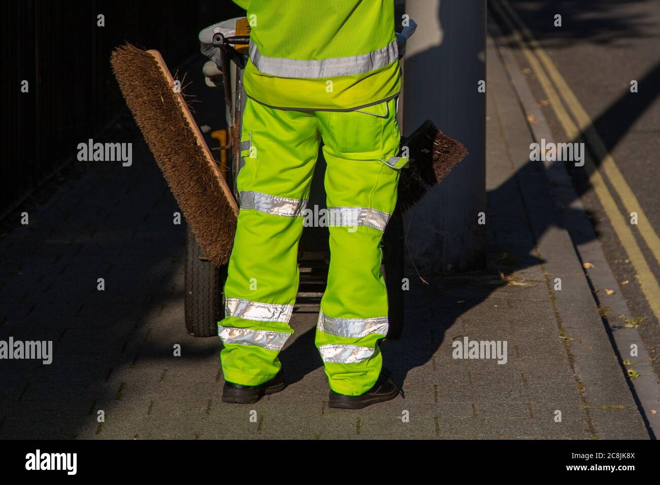 A road sweeper sweeping the street wearing high visibility trousers Stock Photo