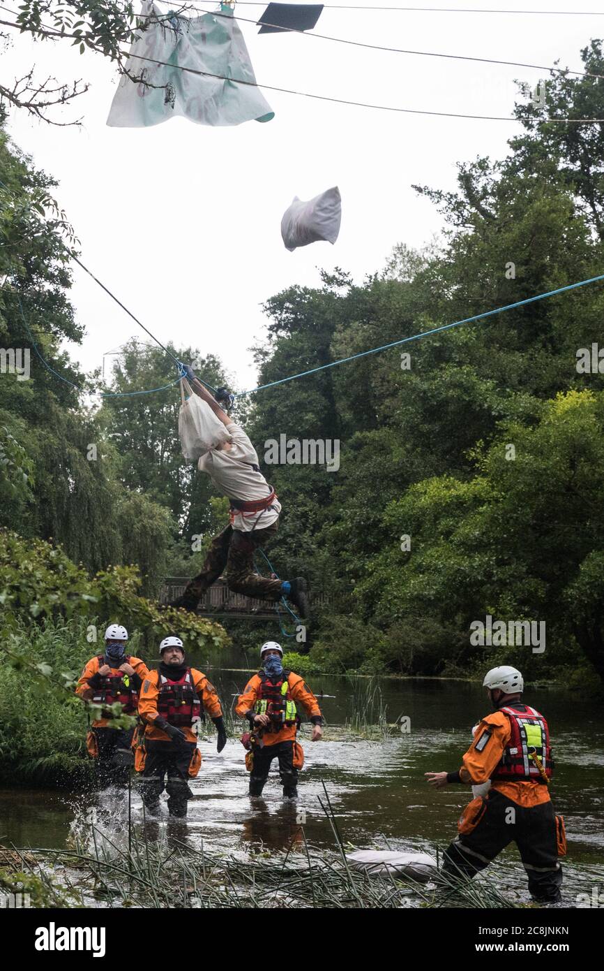 Denham, UK. 24 July, 2020. Swan, an environmental activist from HS2 Rebellion, and her possessions fall suddenly as her safety line above the shallow river Colne is released by police officers from an ancient alder tree to which she had been attached for almost fourteen hours in an attempt to protect it from destruction during works for the HS2 high-speed rail link. Officers from Hampshire Police Marine Support Unit look on. An activist had been hospitalised when a safety line had been released in this way the previous day. Credit: Mark Kerrison/Alamy Live News Stock Photo
