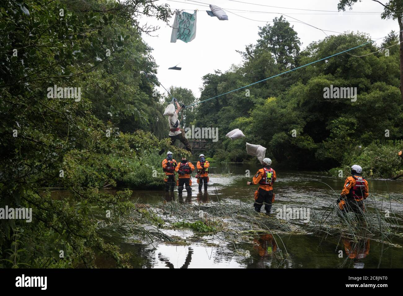 Denham, UK. 24 July, 2020. Swan, an environmental activist from HS2 Rebellion, and her possessions fall suddenly as her safety line above the shallow river Colne is released by police officers from an ancient alder tree to which she had been attached for almost fourteen hours in an attempt to protect it from destruction during works for the HS2 high-speed rail link. Officers from Hampshire Police Marine Support Unit look on. An activist had been hospitalised when a safety line had been released in this way the previous day. Credit: Mark Kerrison/Alamy Live News Stock Photo