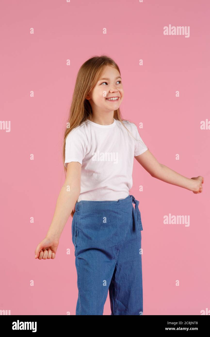 A little girl of 7 years in a white shirt on a pink background, emotions of joy and happiness. copy space. Stock Photo