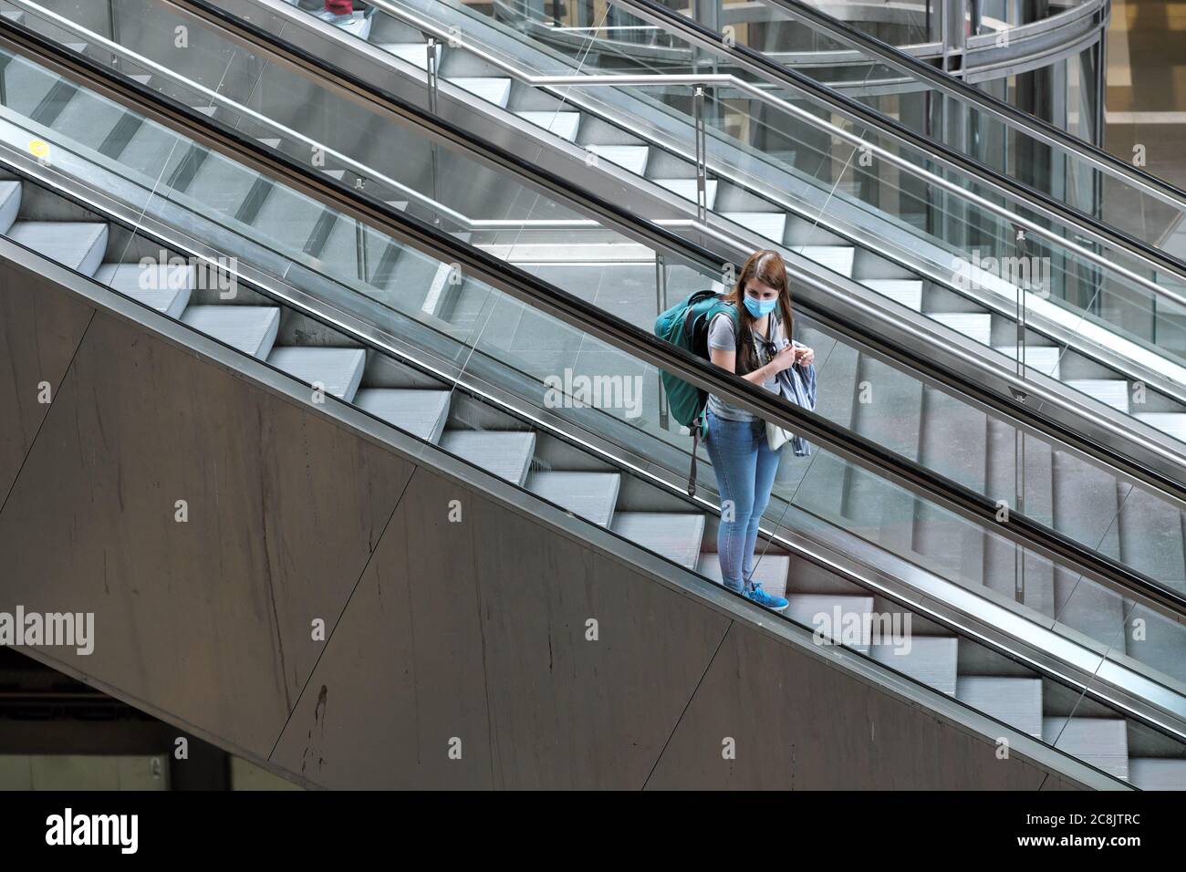 Berlin Germany a lone female visitor with backpack and coronavirus facemask travels on an escalator at Berlin Hauptbahnhof railway station July 2020 Stock Photo