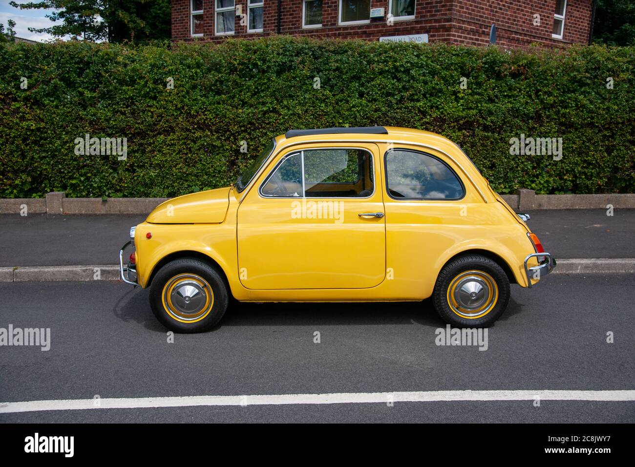 Yellow 1971 Fiat 500 two-door saloon parked on Sixties council estate side street Stock Photo