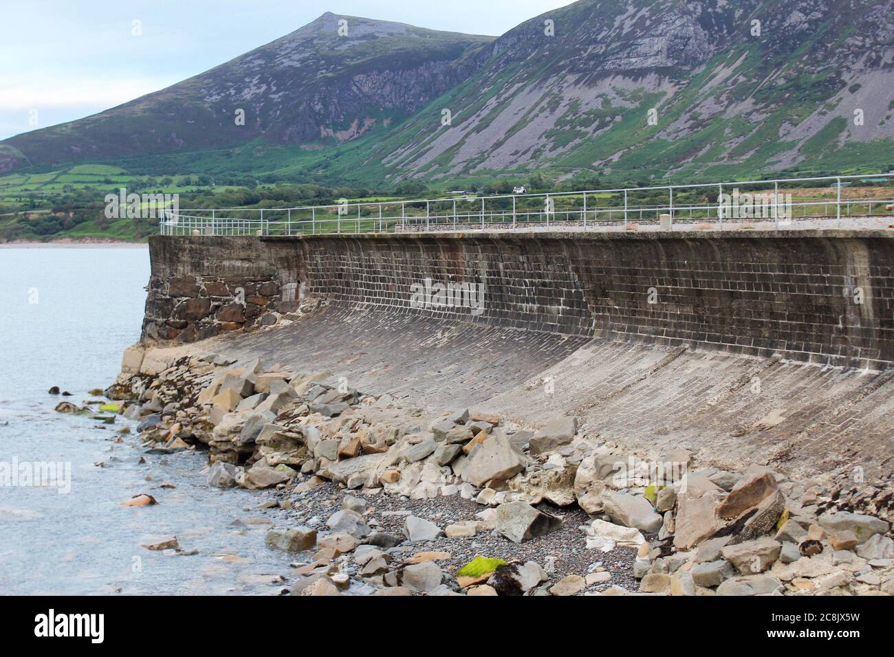 Old curved sea wall with rock armour sea defence, inc the rivals mountains (Yr Eifl) at Trefor, North Wales Stock Photo