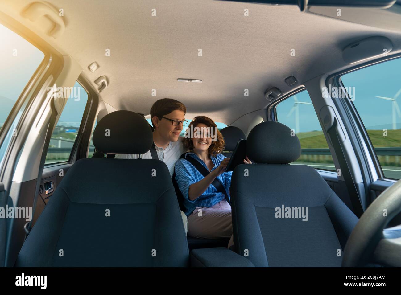 Passengers sit in the back seat and look at the digital tablet while self-driving car rides on the highway. Stock Photo