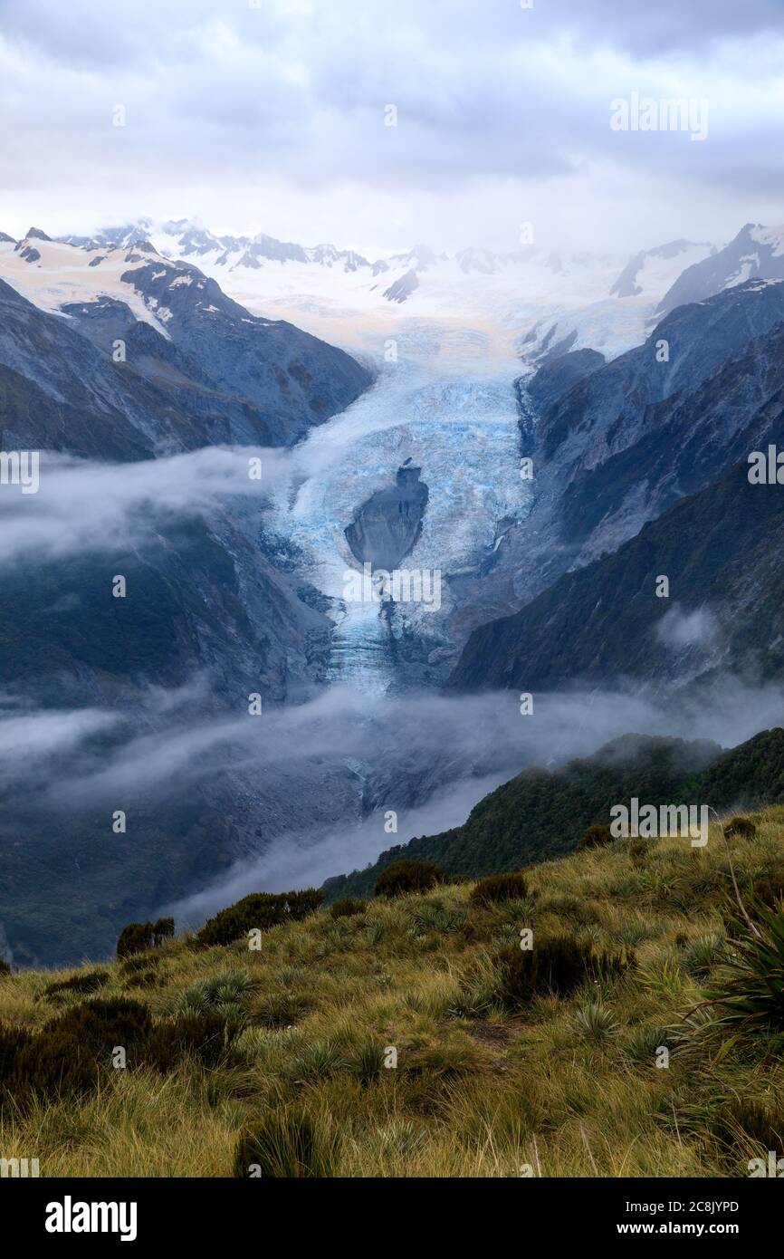 Franz Josef Glacier with wispy clouds in front of it it. After sunset, at dusk, from the view of the summit of Alex Knob. Franz Josef Glacier, South I Stock Photo