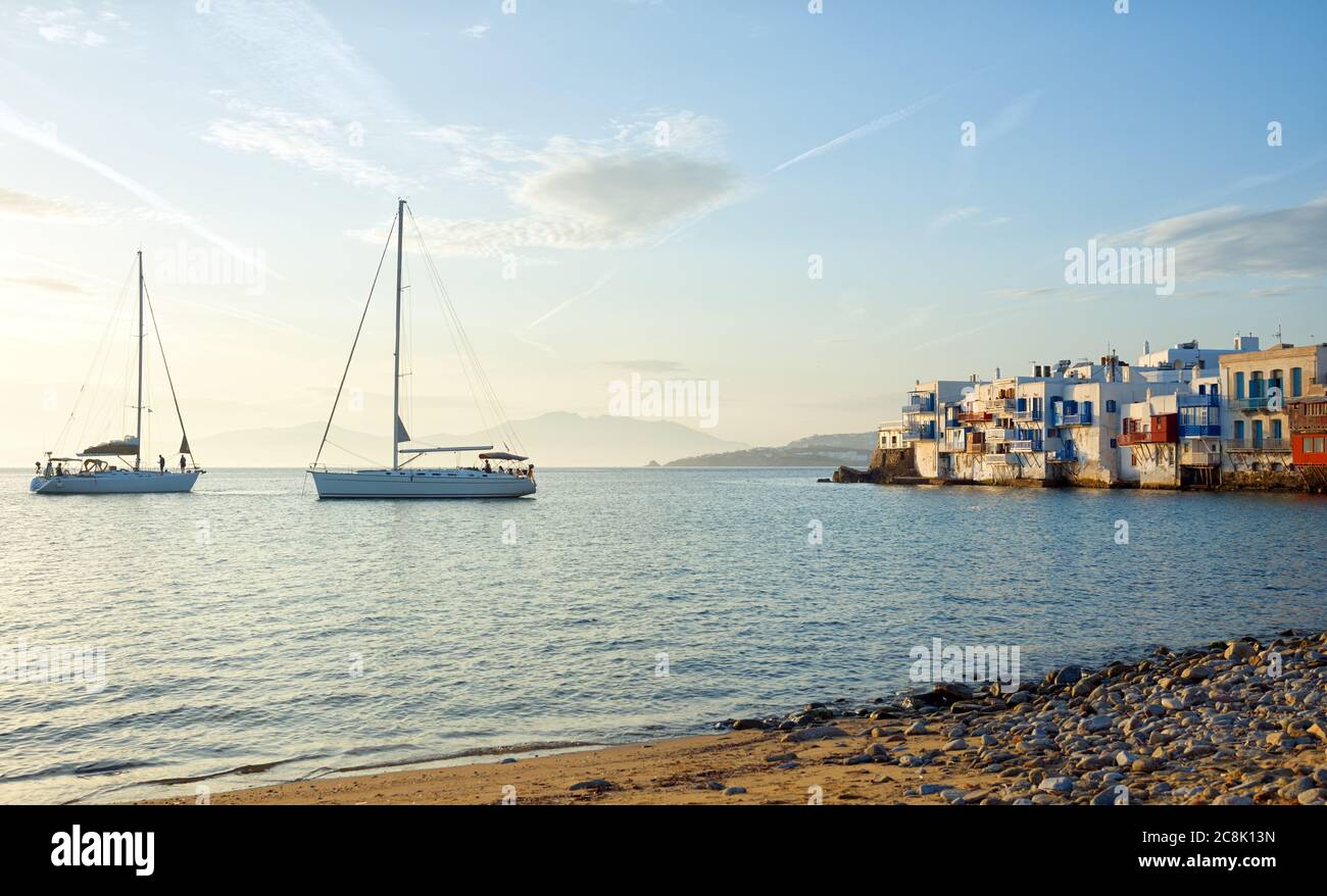 Two yachts at sea next to varicolored houses of Mykonos, Greece Stock Photo