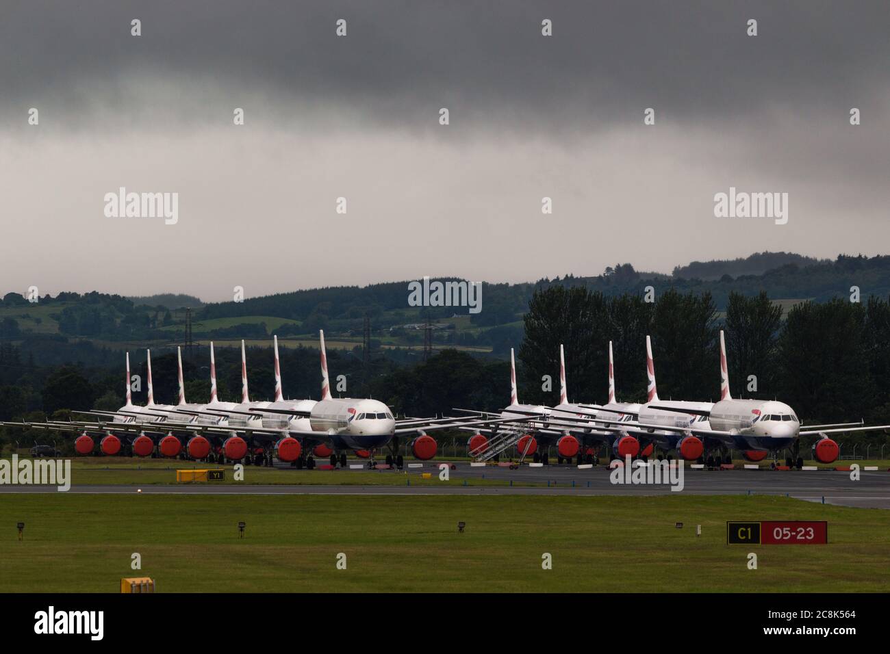 Glasgow, Scotland, UK. 23 July 2020. Pictured: Under a threatening dark stormy cloud, grounded British Airways (BA) Airbus A319/A320/A321 aircraft sit the second runway of Glasgow Airport awaiting their fate of being sold off or put in storage.  Since March these planes have been sitting idle on the the airports tarmac, doe to the global coronavirus (COVID19) crisis.  British Airways have cut almost 12,000 staff, and to date have retired their whole Boeing 747 fleet in a bid to cut operating costs. Credit: Colin Fisher/Alamy Live News. Stock Photo