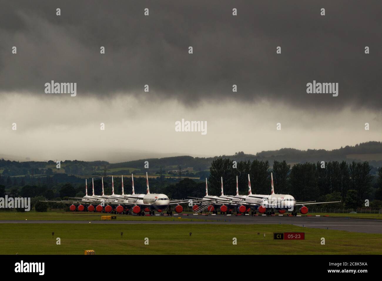 Glasgow, Scotland, UK. 23 July 2020. Pictured: Under a threatening dark stormy cloud, grounded British Airways (BA) Airbus A319/A320/A321 aircraft sit the second runway of Glasgow Airport awaiting their fate of being sold off or put in storage.  Since March these planes have been sitting idle on the the airports tarmac, doe to the global coronavirus (COVID19) crisis.  British Airways have cut almost 12,000 staff, and to date have retired their whole Boeing 747 fleet in a bid to cut operating costs. Credit: Colin Fisher/Alamy Live News. Stock Photo